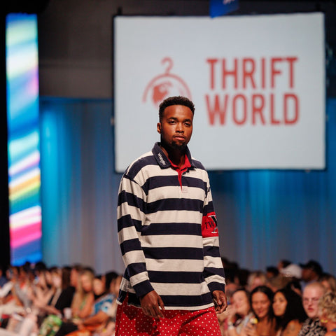 Model walking on a runway wearing a striped shirt and red pants with 'Thrift World' branding in the background.