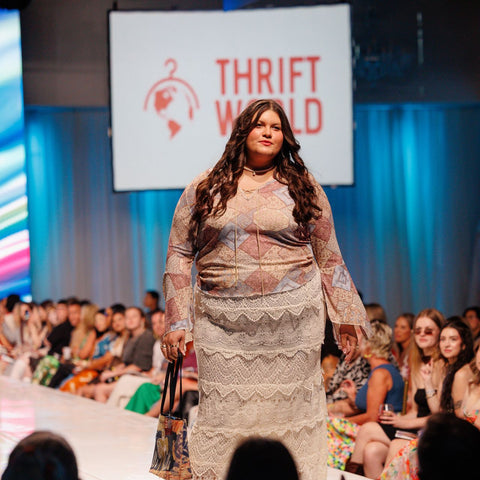 Model walking on a fashion runway with 'Thrift World' branding in the background.